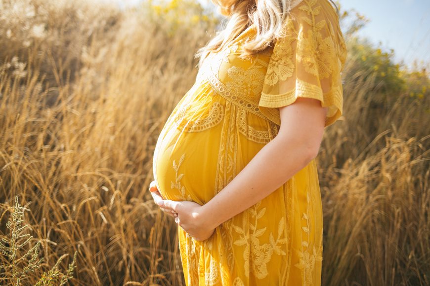 Pregnant lady in a yellow dress holding her belly